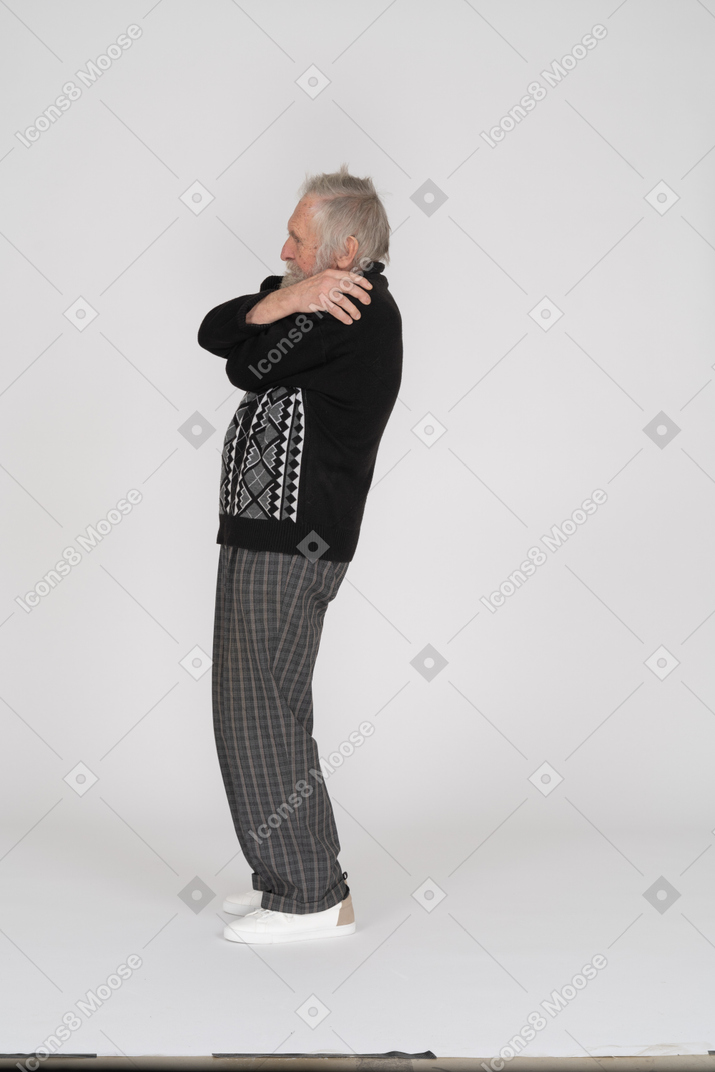 Vista lateral de un anciano abrazándose a sí mismo