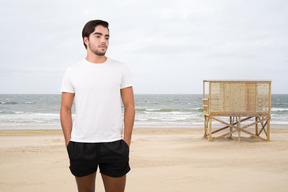 A man standing on a beach with a lifeguard hut