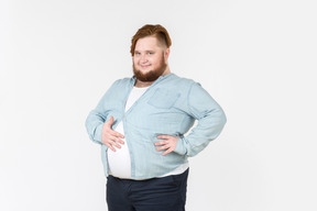 Young overweight man in tight shirt holding hand on belly