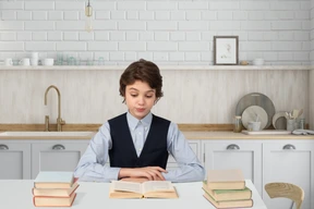 A schoolboy sitting at a table and reading a book