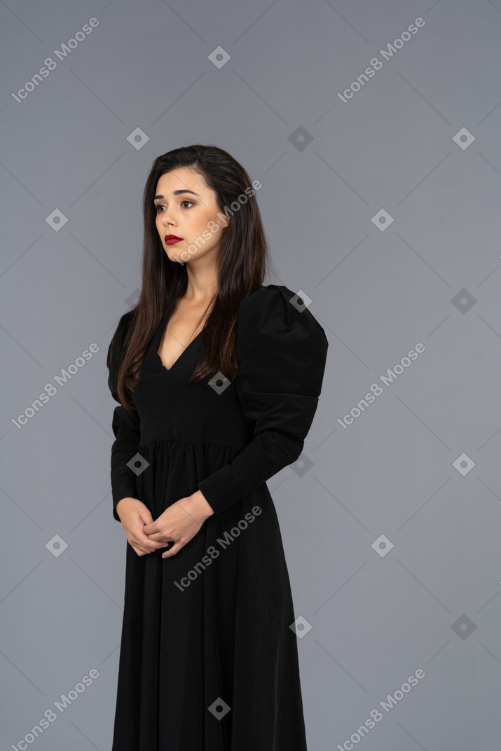 Трехчетвертный вид молодой девушки в черном платье, стоящей на месте