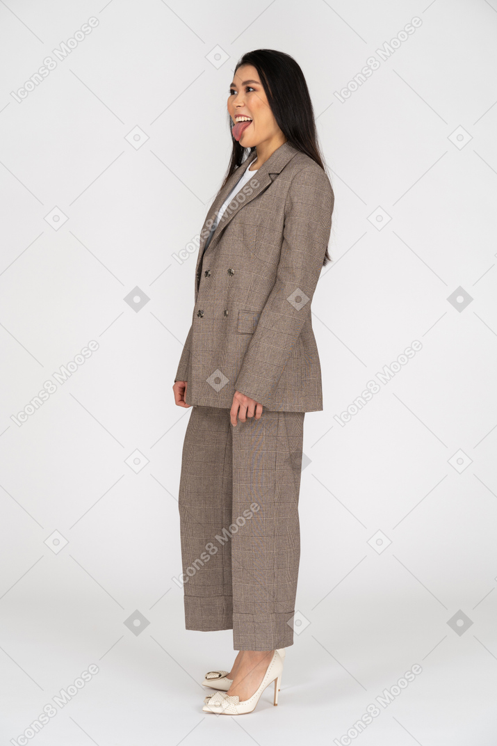 Вид в три четверти молодой леди в коричневом деловом костюме, показывающей язык