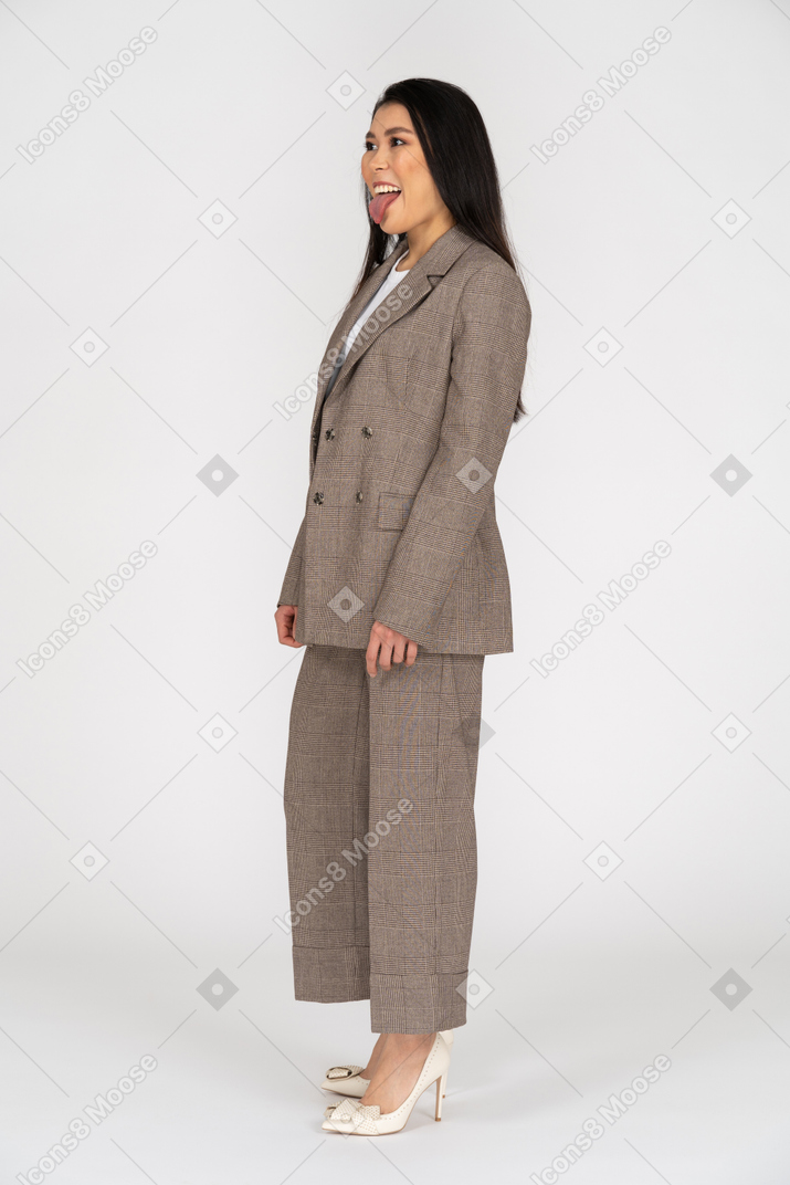 Vue de trois quarts d'une jeune femme en costume marron montrant la langue