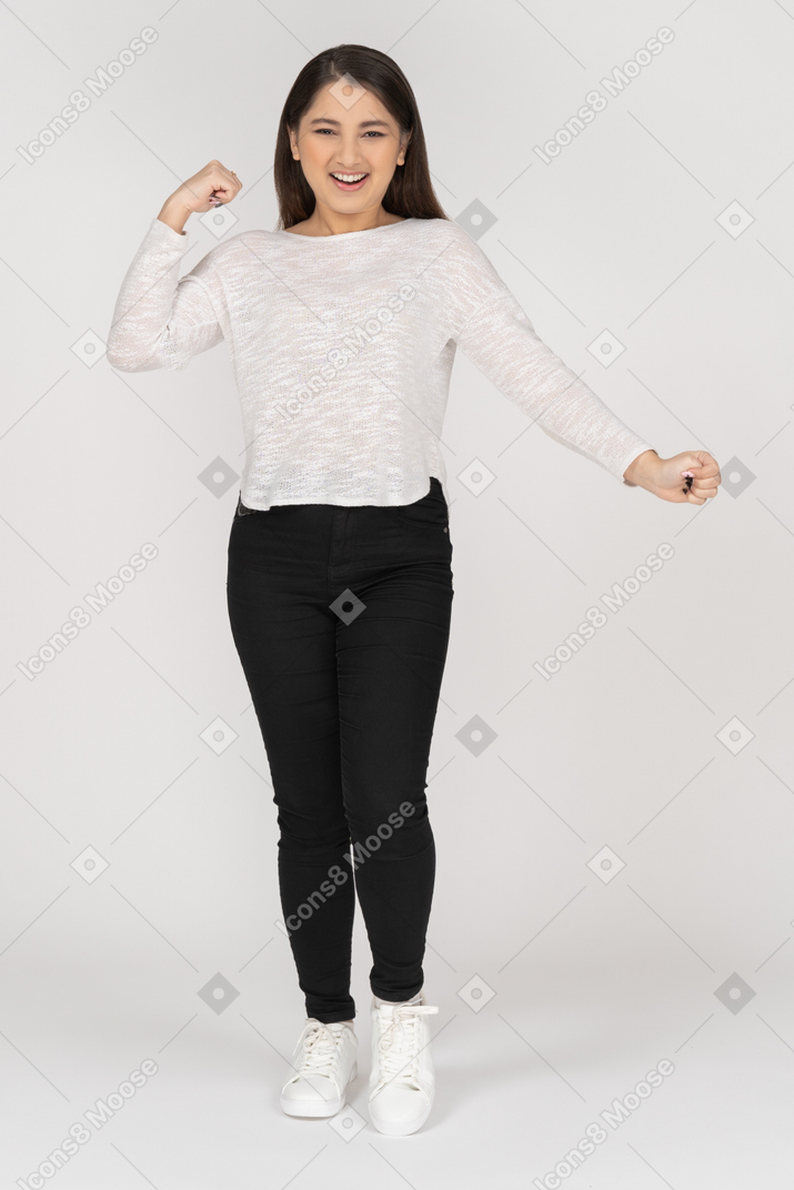 Front view of a smiling young dancing indian female in casual clothes raising hand