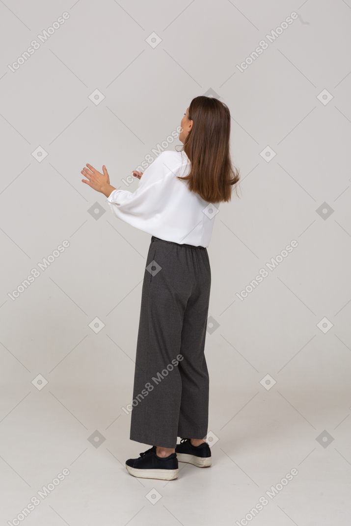 Three-quarter back view of a shocked young lady in office clothing raising hands