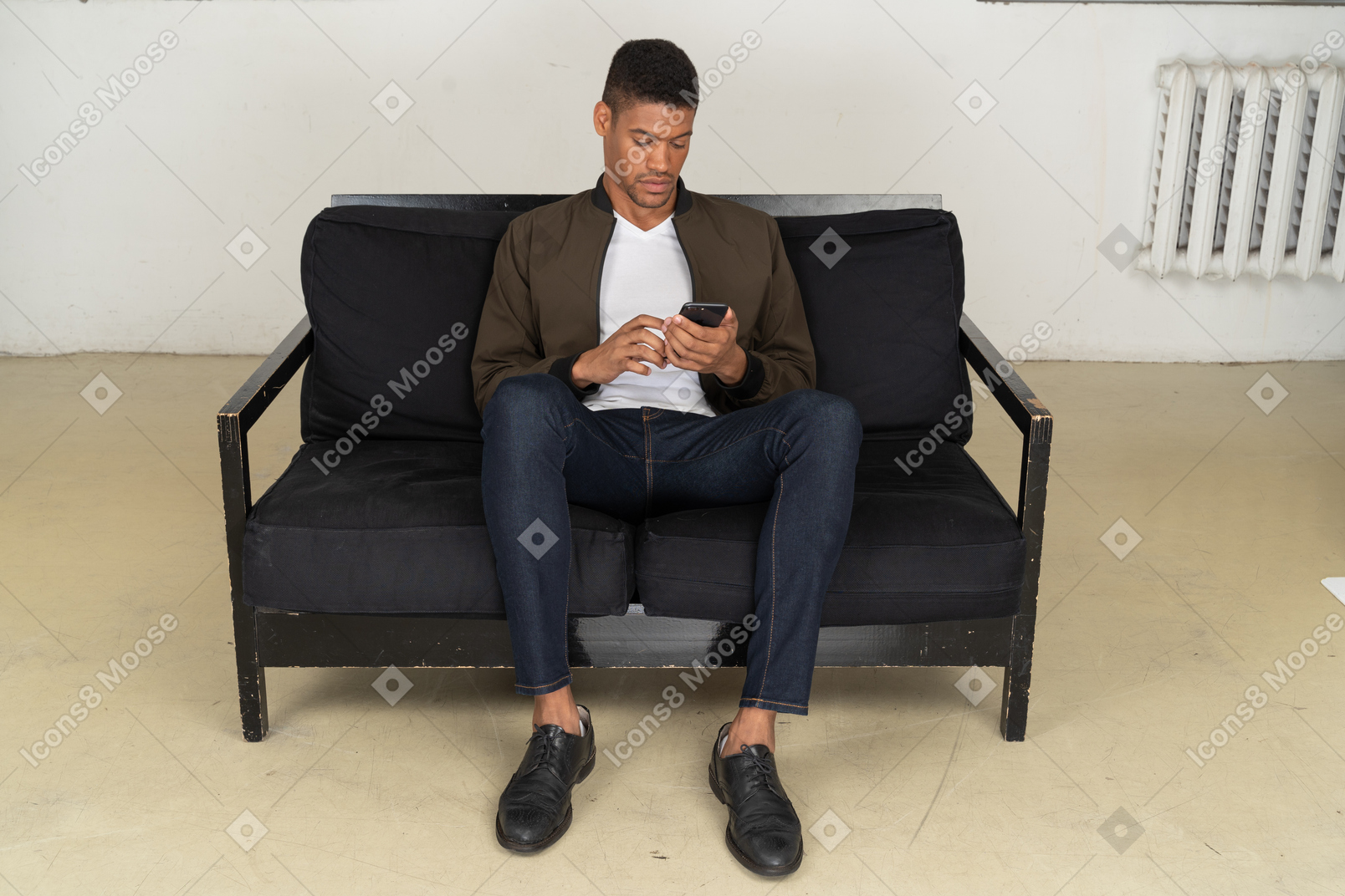 ソファに座って彼の電話を見ている若い男の正面図