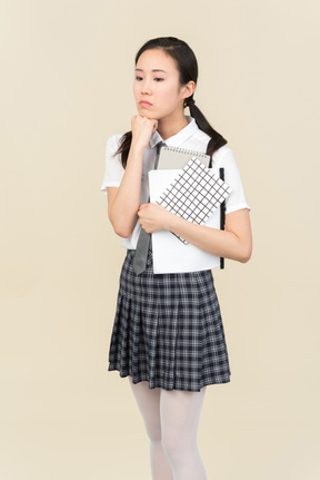 Triste olhando menina da escola asiática segurando notas