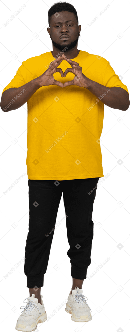 Vista frontale di un cupo giovane uomo dalla pelle scura in maglietta gialla che mostra il gesto del cuore