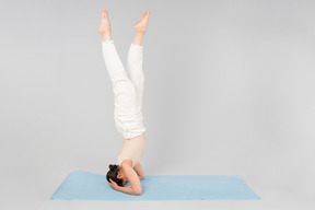 Young indian woman standing on the head on yoga mat