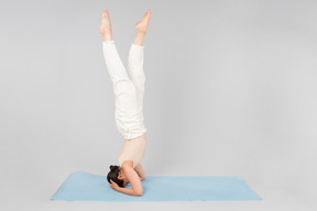 Jeune femme indienne debout sur la tête sur un tapis de yoga