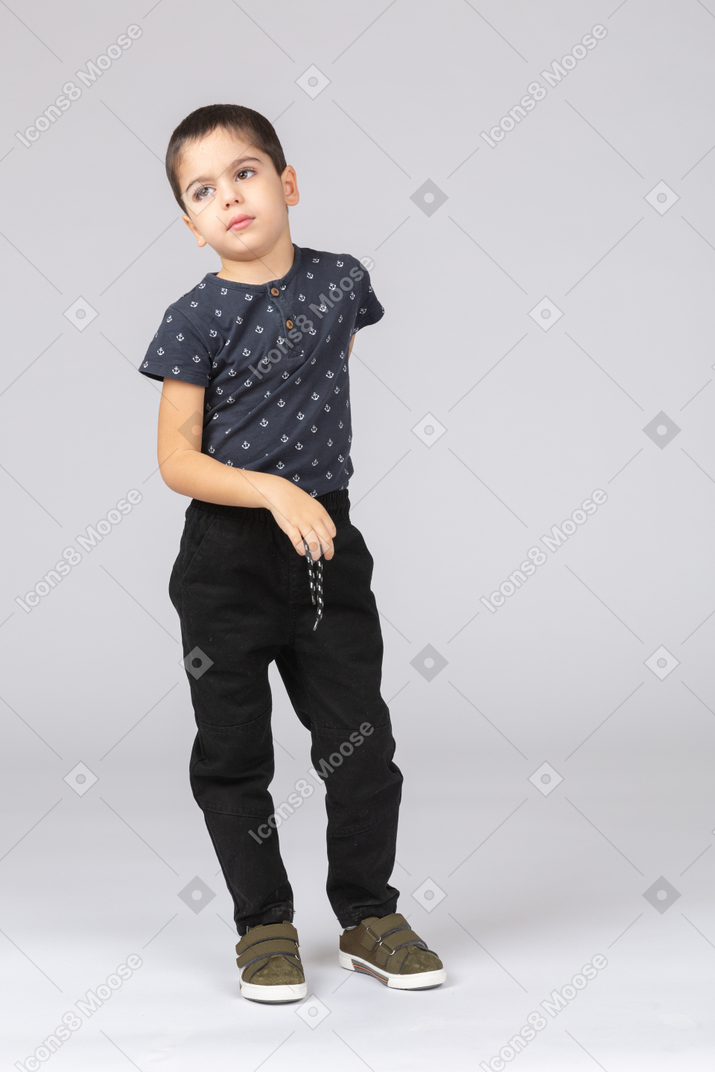 Vue de face d'un garçon mignon posant avec le bras derrière le dos