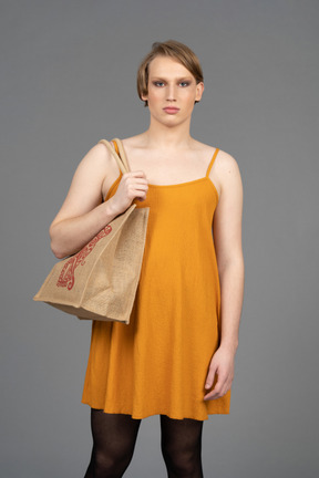 Portrait of a young transgender person in orange dress carrying bag