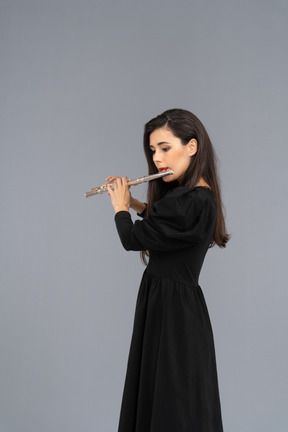 フルートを演奏する黒いドレスを着た真面目な若い女性の側面図