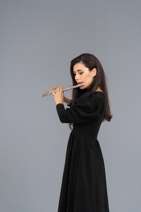 Side view of a serious young lady in black dress playing the flute