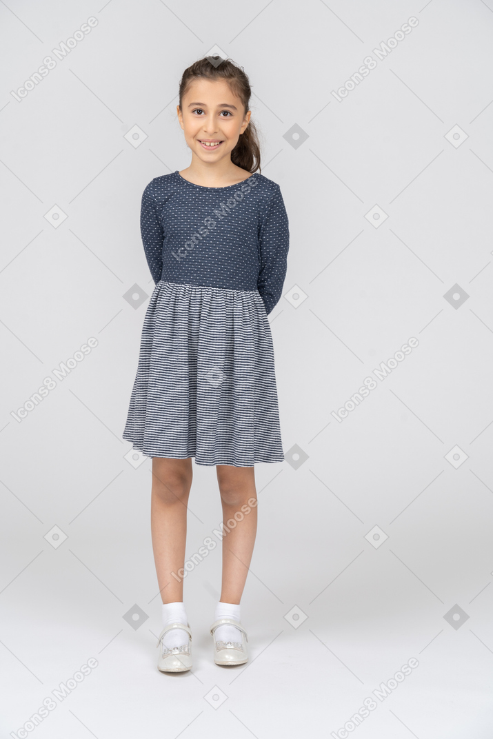 Vista frontal de uma garota sorrindo timidamente com as mãos atrás das costas