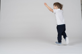 Vista trasera de un niño corriendo con las manos levantadas