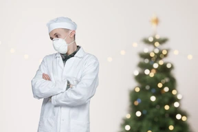 A man wearing a surgical mask standing in front of a christmas tree