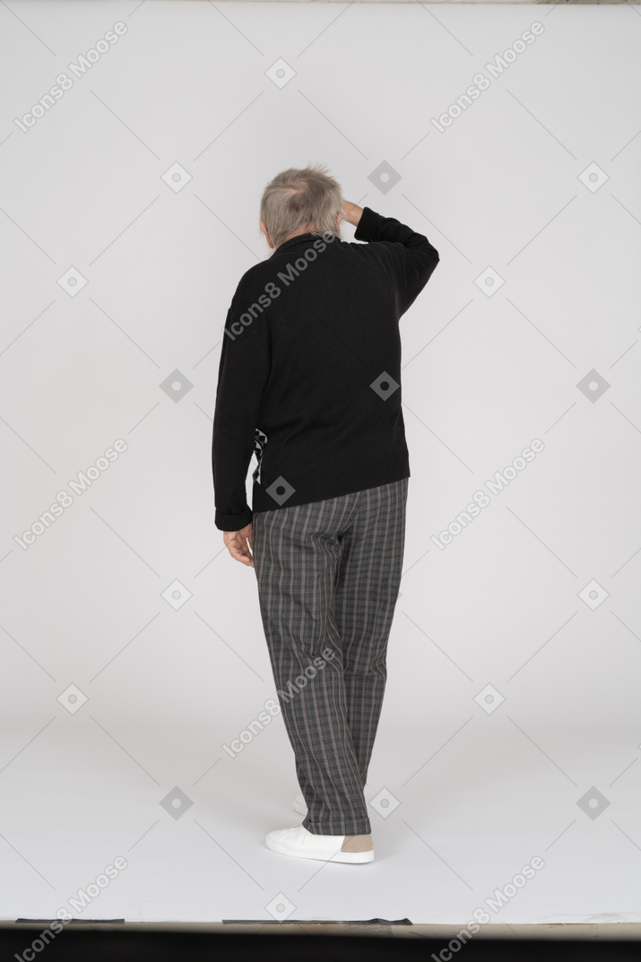 Back view of old man standing with hand on forehead