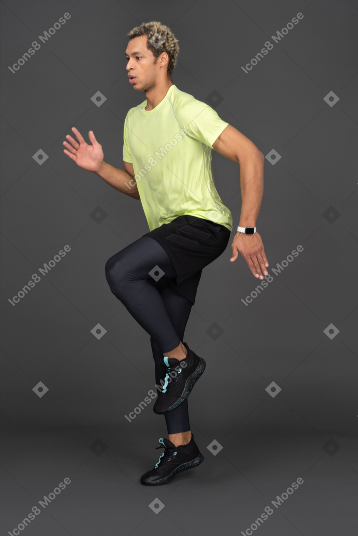 Three-quarter view of a jumping dark-skinned young man raising hand and bending knee