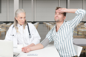 Doctor checking blood pressure of dramatizing man