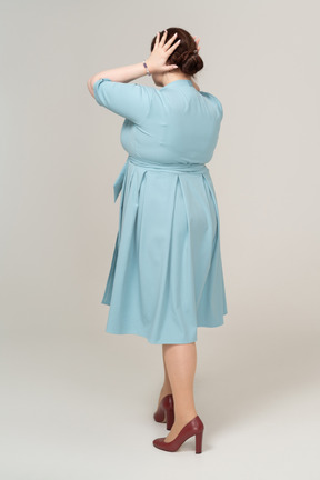 一个穿着蓝色连衣裙的女人用手捂住耳朵的后视图