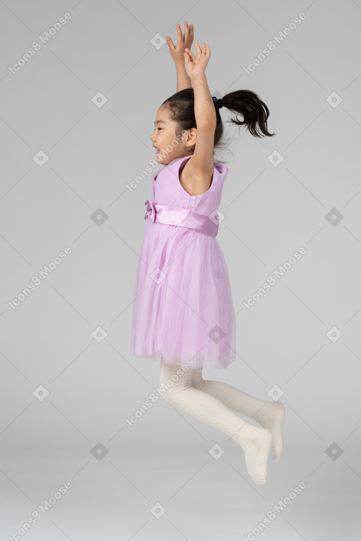 Chica con un vestido rosa saltando con los brazos arriba