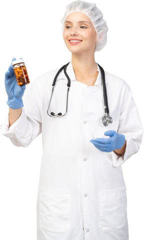 Vista frontal de una sonriente joven doctora sosteniendo un frasco de pastillas