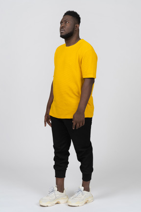 Vista di tre quarti di un giovane uomo dalla pelle scura con una maglietta gialla in piedi immobile