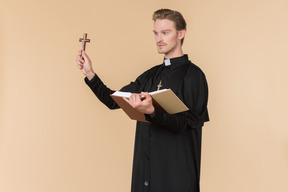 Catholic priest holding cross and reading a bible