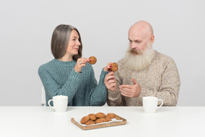 Ältere frau, die einen von zwei plätzchen gibt, die sie zum älteren mann hält