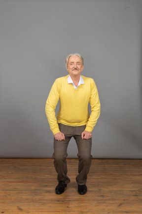 Front view of an old squatting man in a yellow pullover looking aside