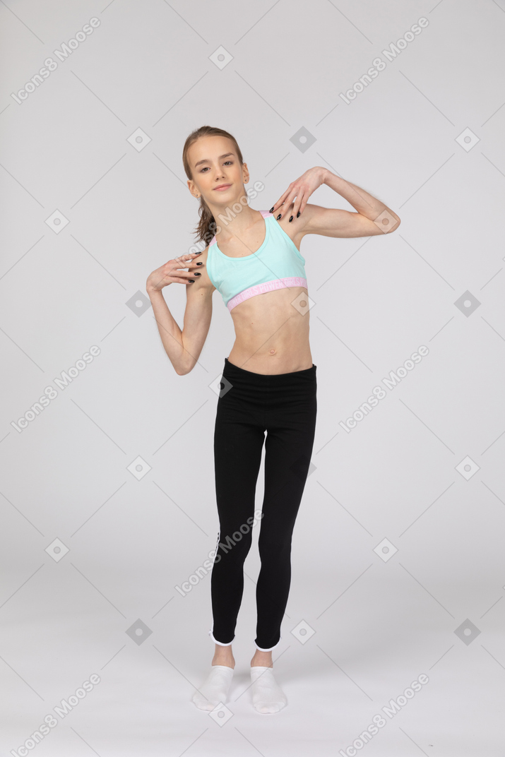 Front view of a teen girl in sportswear touching her shoulders and tilting left