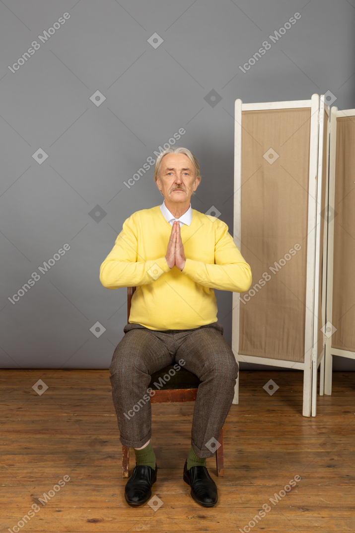 Mann mittleren alters sitzt und hält seine hände im gebet