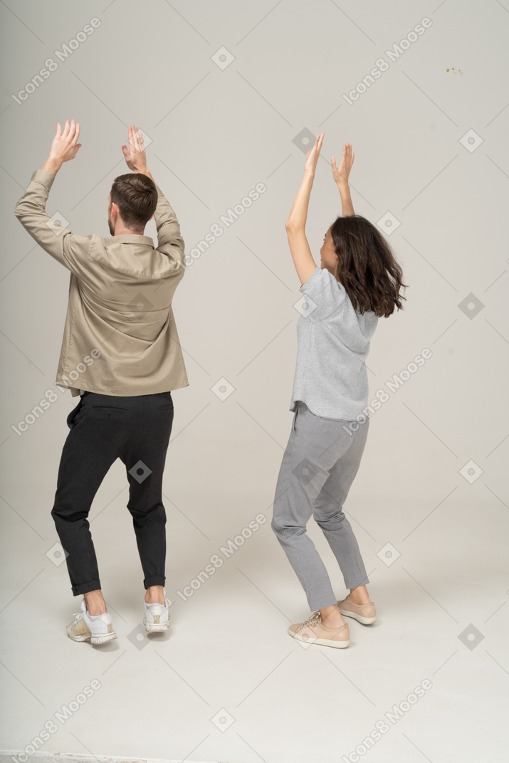 Вид сзади на молодых мужчину и женщину, машущих руками в три четверти