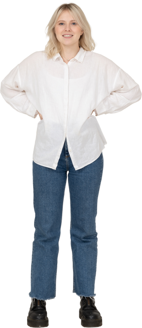 Vista frontale di una donna bionda in abiti casual, mettendo le mani sui fianchi e guardando la fotocamera