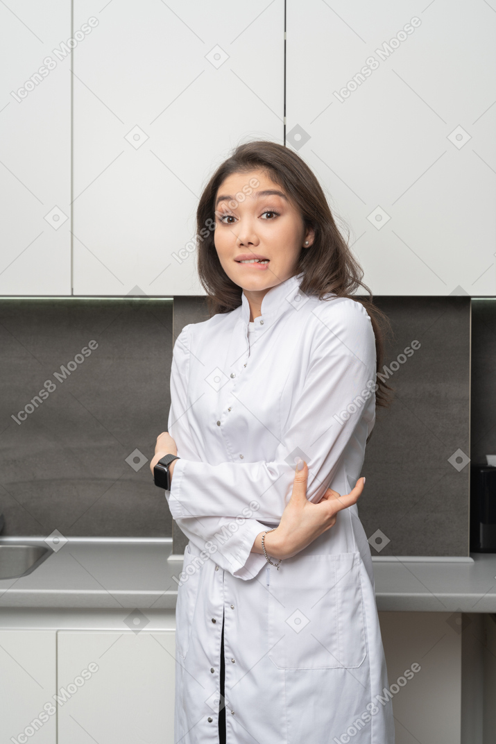 Front view of a shy female doctor crossing hands and biting lips