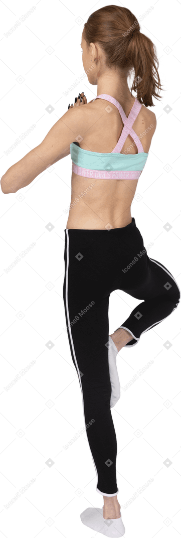 Dreiviertel-rückansicht eines jugendlichen mädchens in der sportbekleidung, die auf einem bein balanciert und hände zusammenhält