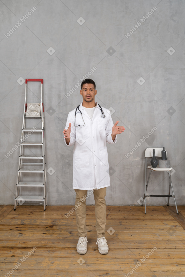 Vista frontal de um jovem médico em uma sala com escada e cadeira mostrando o tamanho de algo