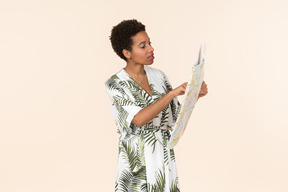 Black short-haired woman in a white and green dress, standing with a map in her hands