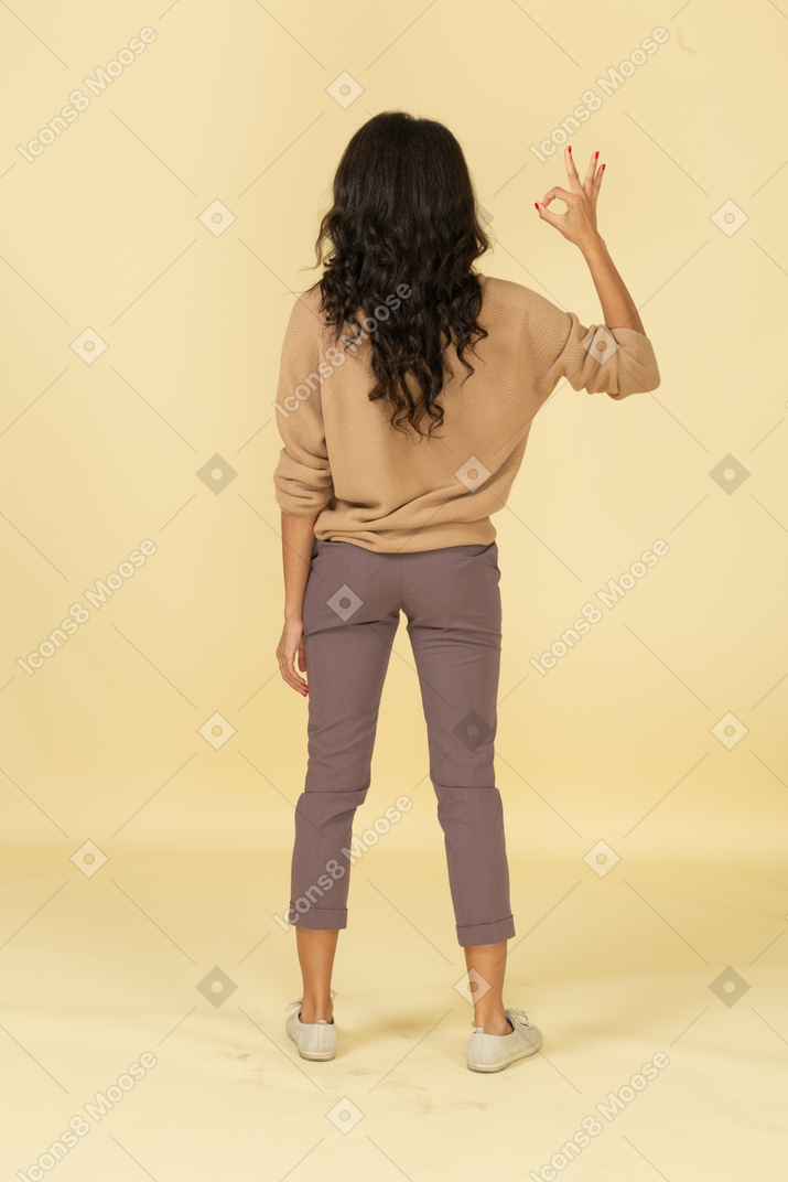 Vista de trás de uma jovem mulher de pele escura mostrando um gesto de ok