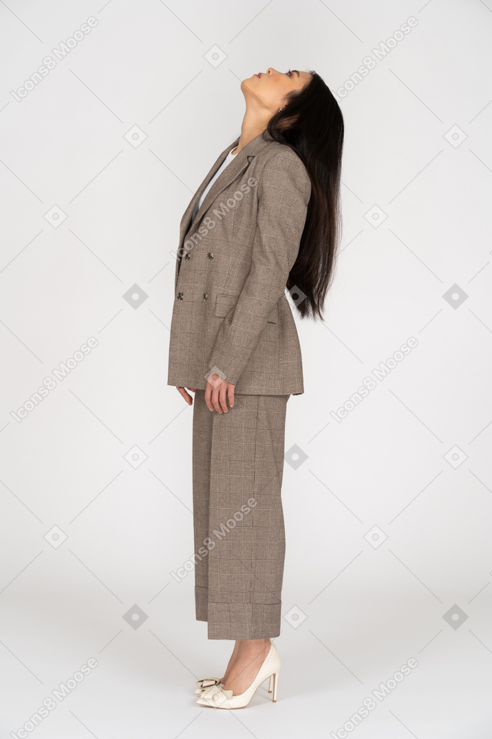 Vista lateral de una señorita en traje marrón echando la cabeza hacia atrás