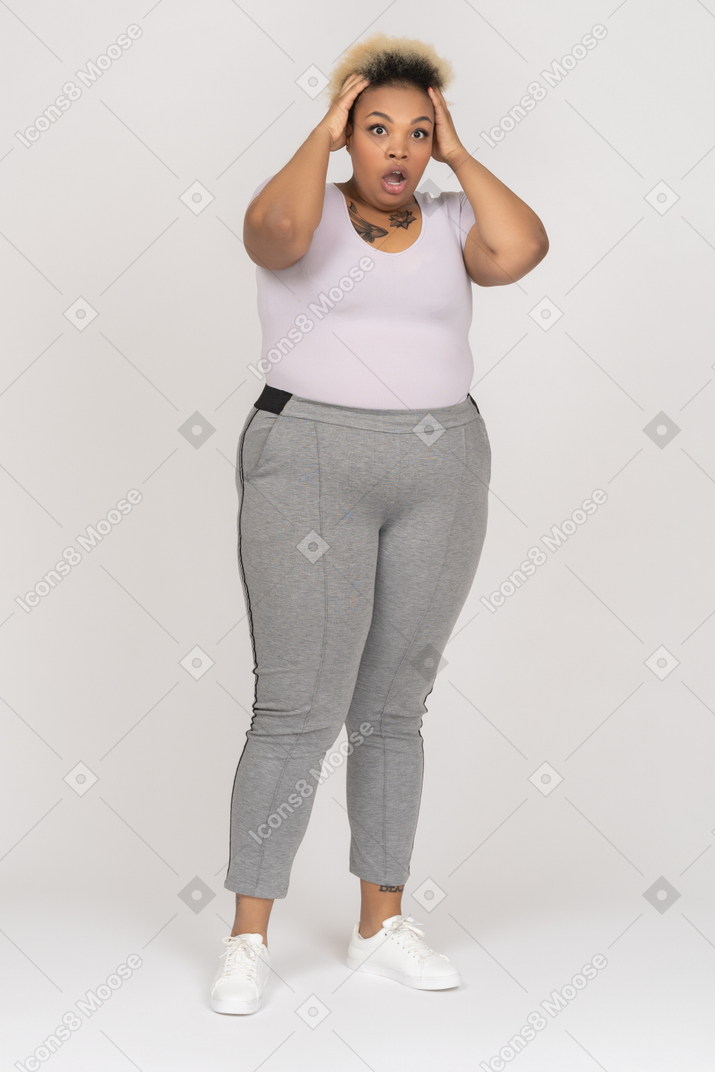 Shocked plump dark skinned female holding head with both hands