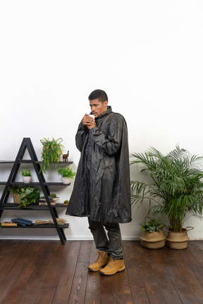 Mann im regenmantel, der versucht, sich mit heißem tee aufzuwärmen