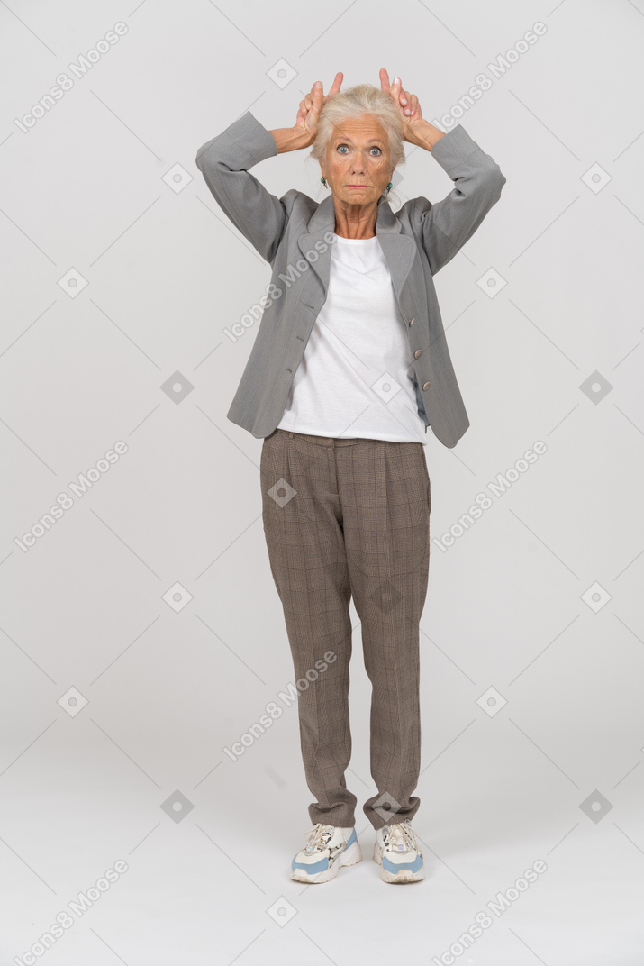 Vista frontale di una vecchia signora in abito che fa le corna