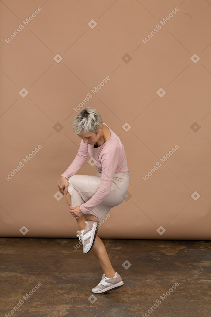 Side view of a woman in casual clothes standing on one leg and touching her shoe