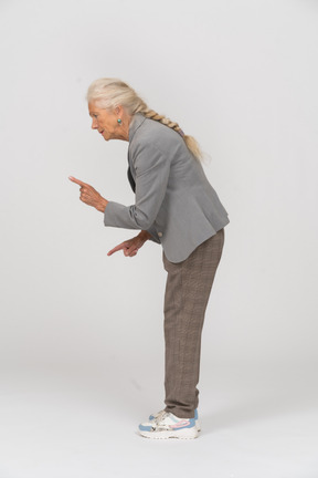 Side view of an old lady in suit bending down and showing warning sign