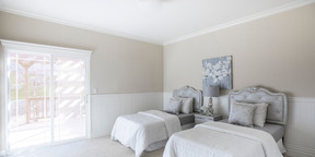 Light-coloured nice bedroom with two classical-looking beds and a painting on the wall, on a bright day