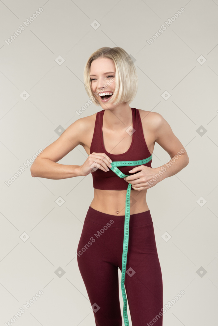 Laughing young woman in sportwear measuring chest