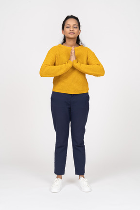 Front view of a girl in casual clothes standing with closed eyes and making praying gesture