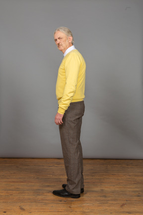 Seitenansicht eines unzufriedenen alten mannes, der gelben pullover trägt und kamera betrachtet